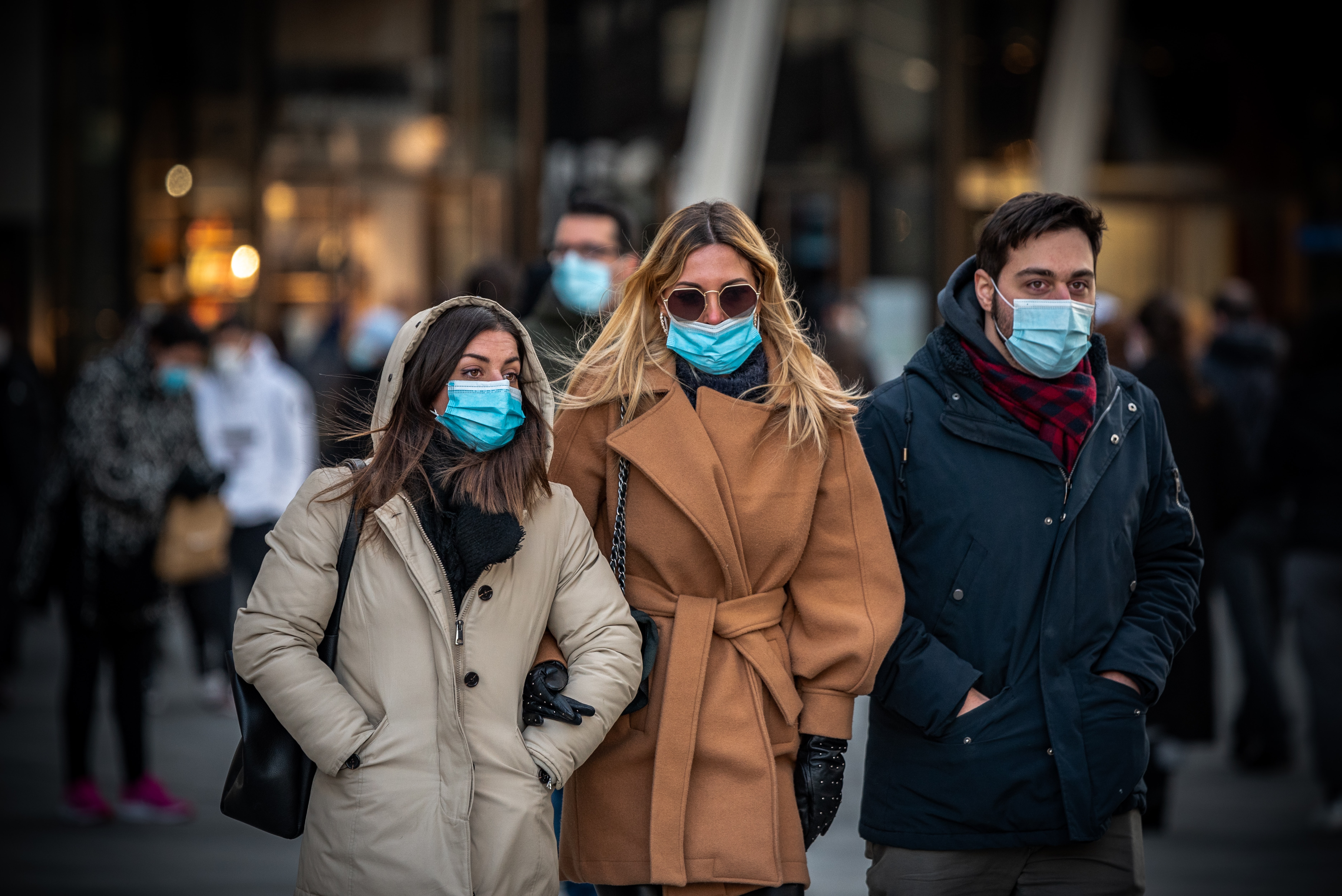 three adults two woman and a man walk down an urban street and wear masks