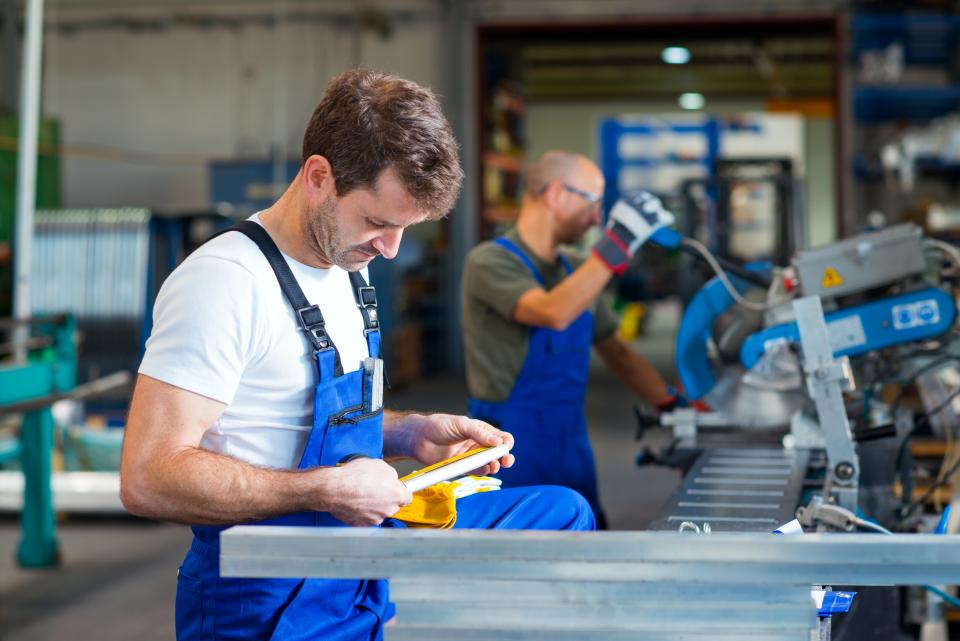 Skilled worker wearing a blue apron is operating a machine in a warehouse
