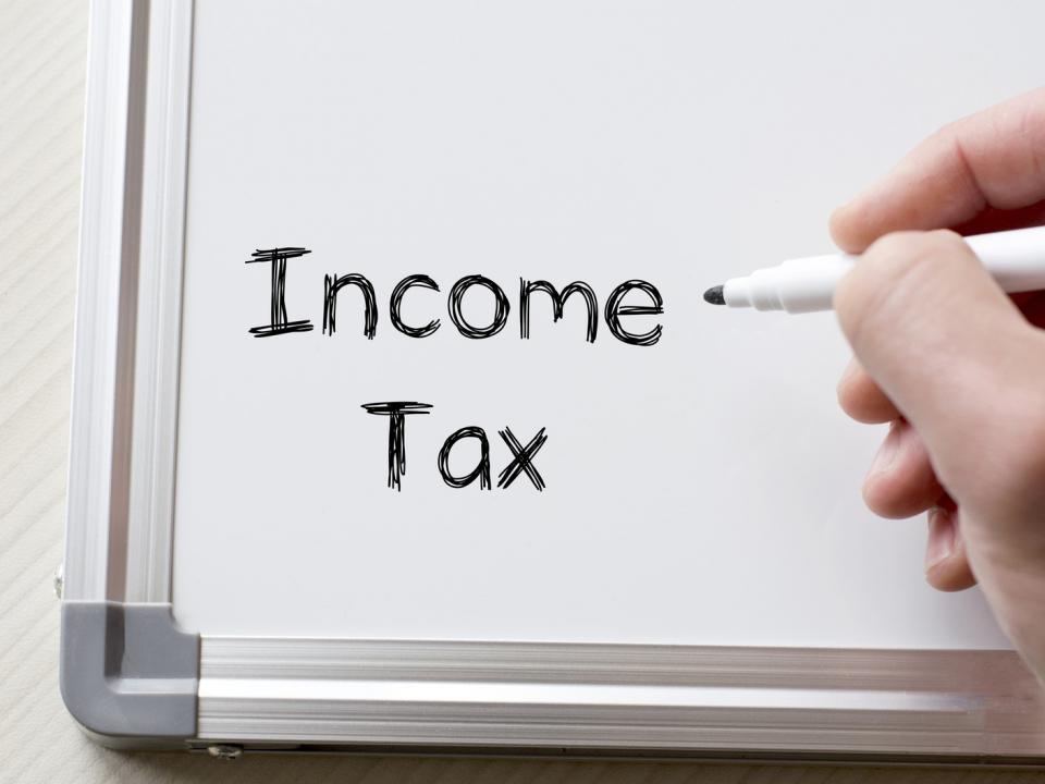 Person writing the words "Income Tax" on a whiteboard
