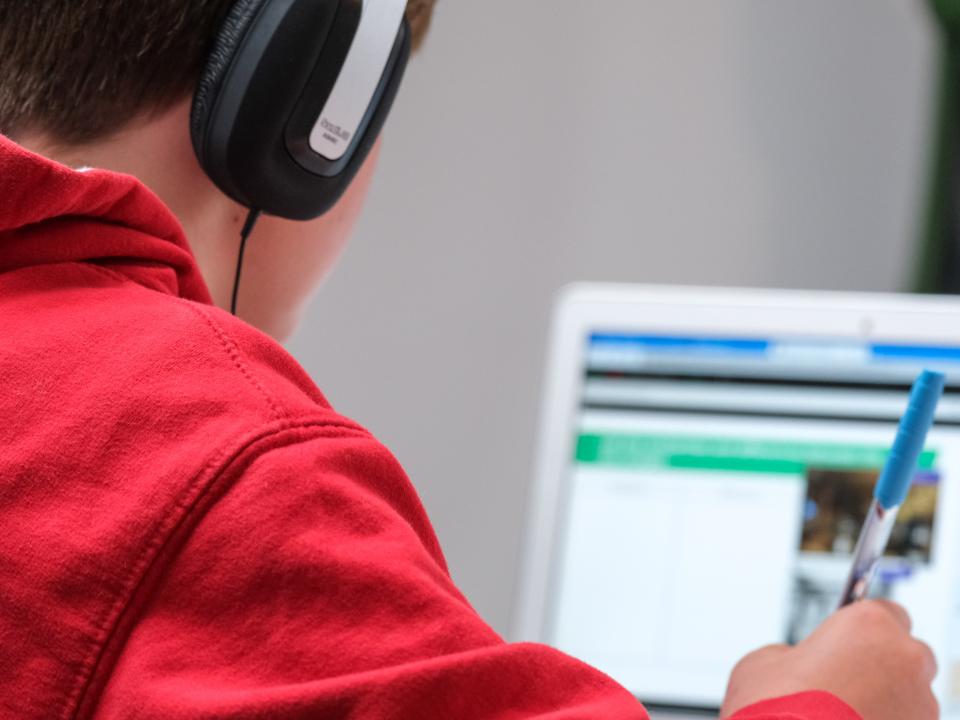 A child is sitting in front of a laptop taking notes