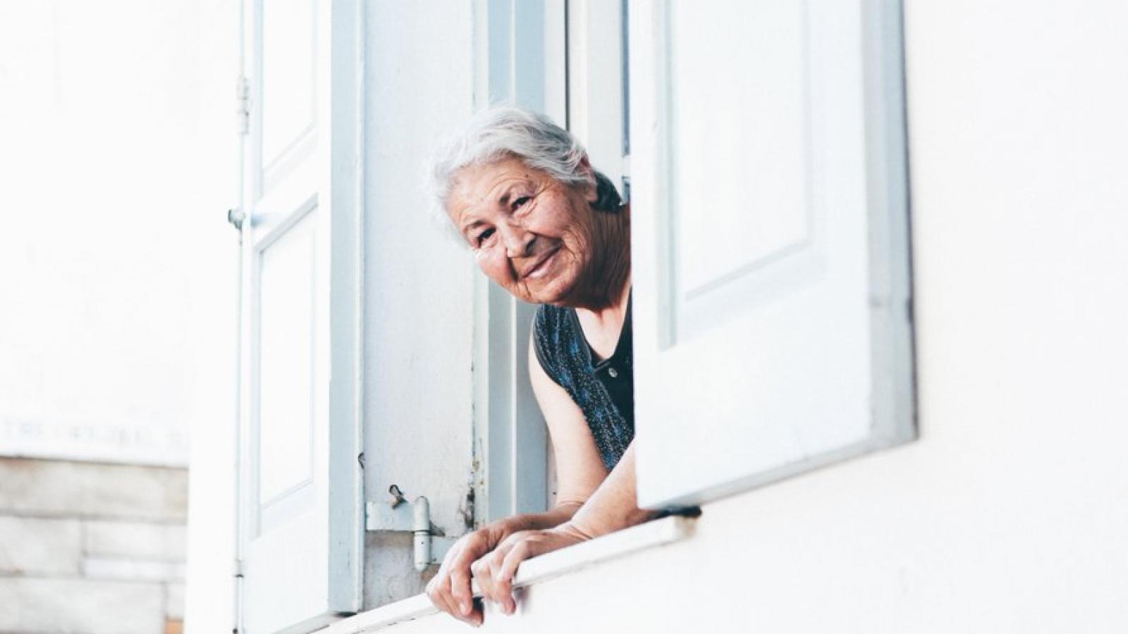 An old lady leans out of a house window and is looking at the camera
