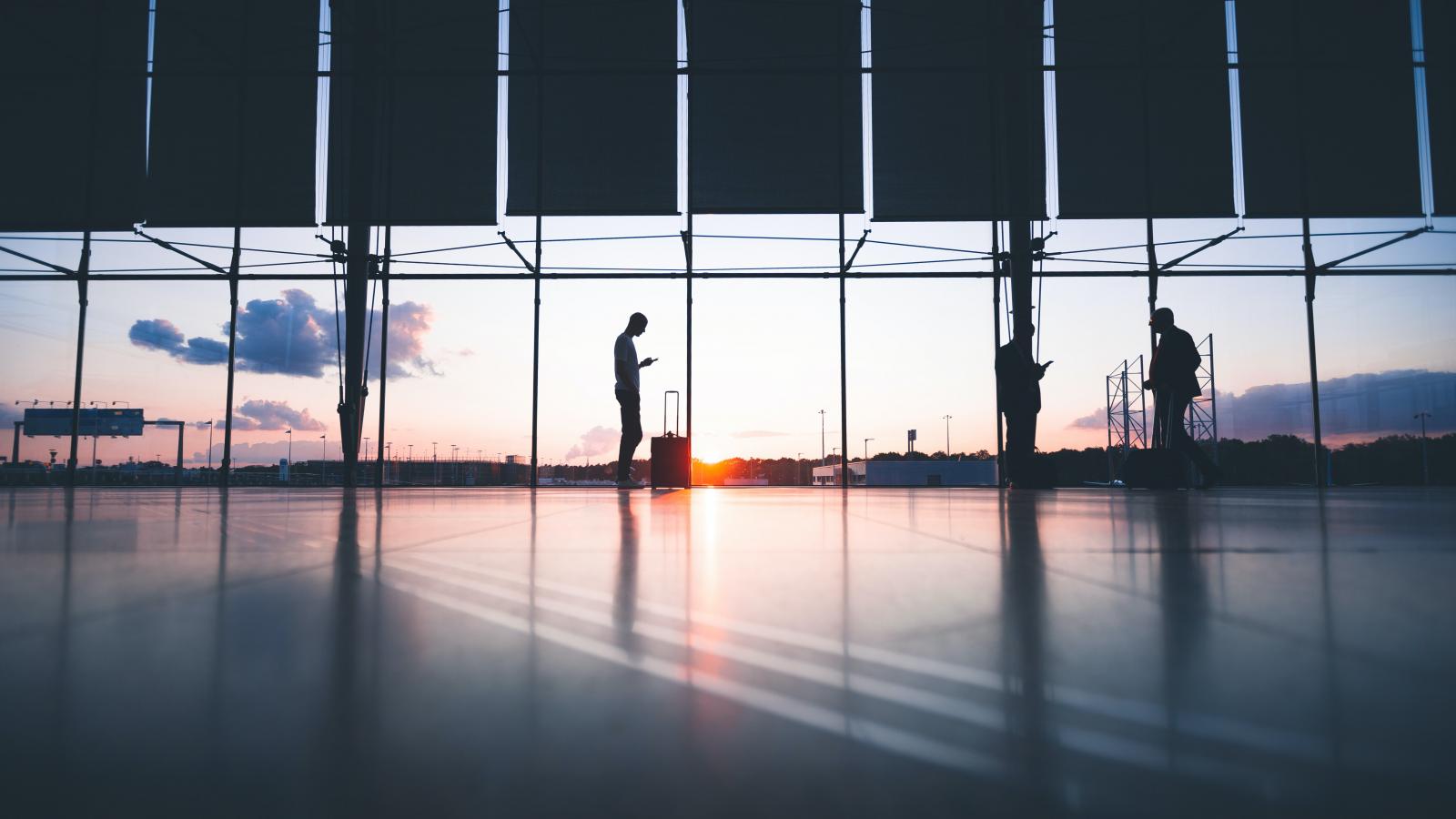 A pair of shadows are standing in a wide airport terminal with a window behind them