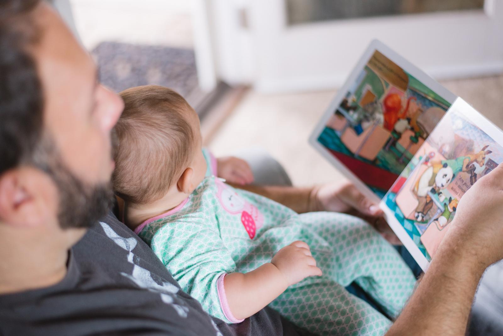 child on a father's lap reading a book together