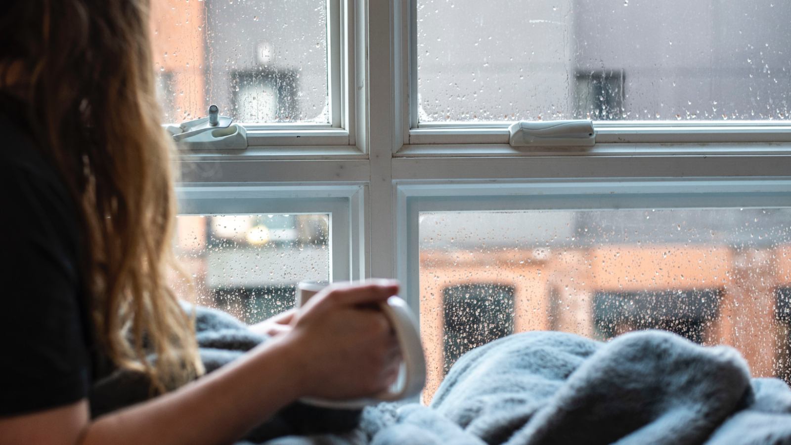woman looking out a window with a mug in her hand