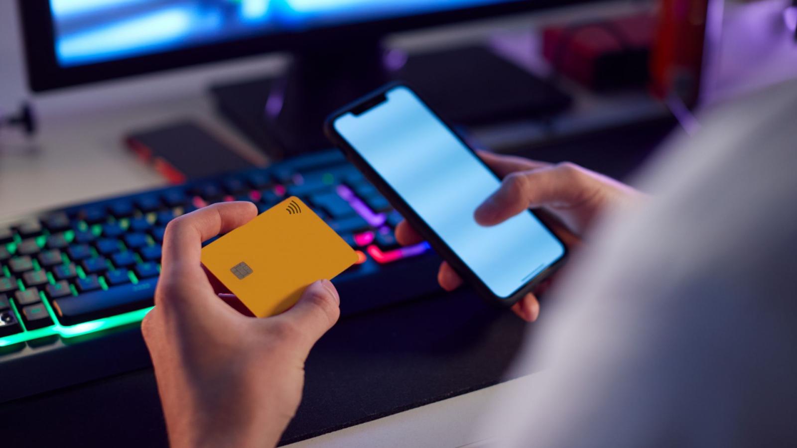 A person holding a credit card and their smartphone, sitting in front of a screen, symbolising online betting.