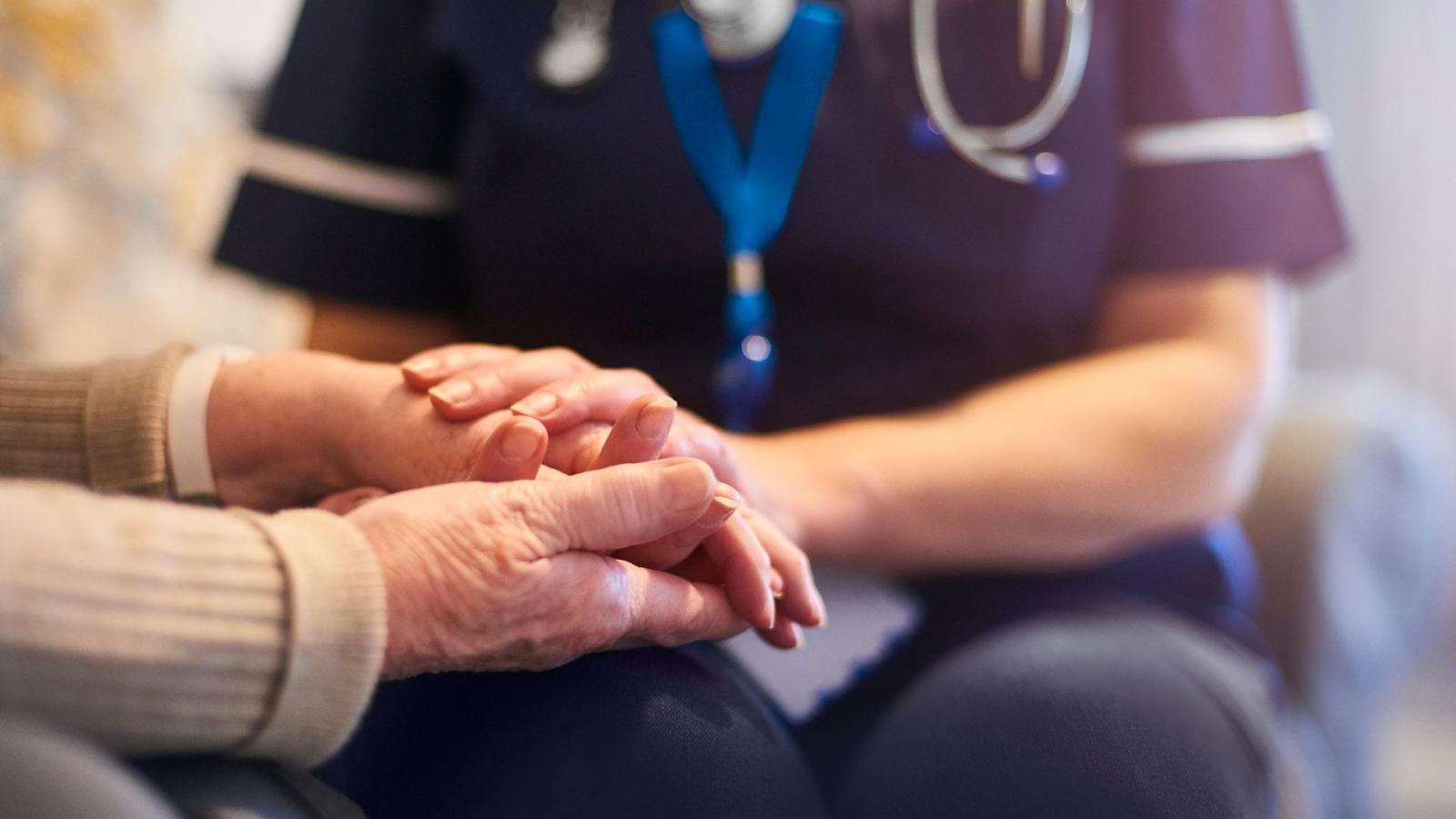 A health worker holding hands of an older person, symbolising care.