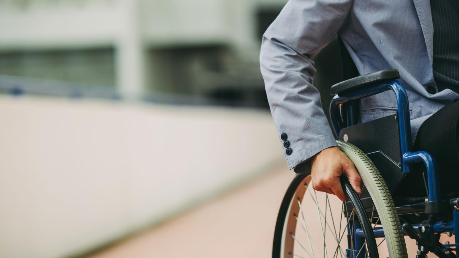 A wheelchair user, holding the wheel of their chair as if they are about to move