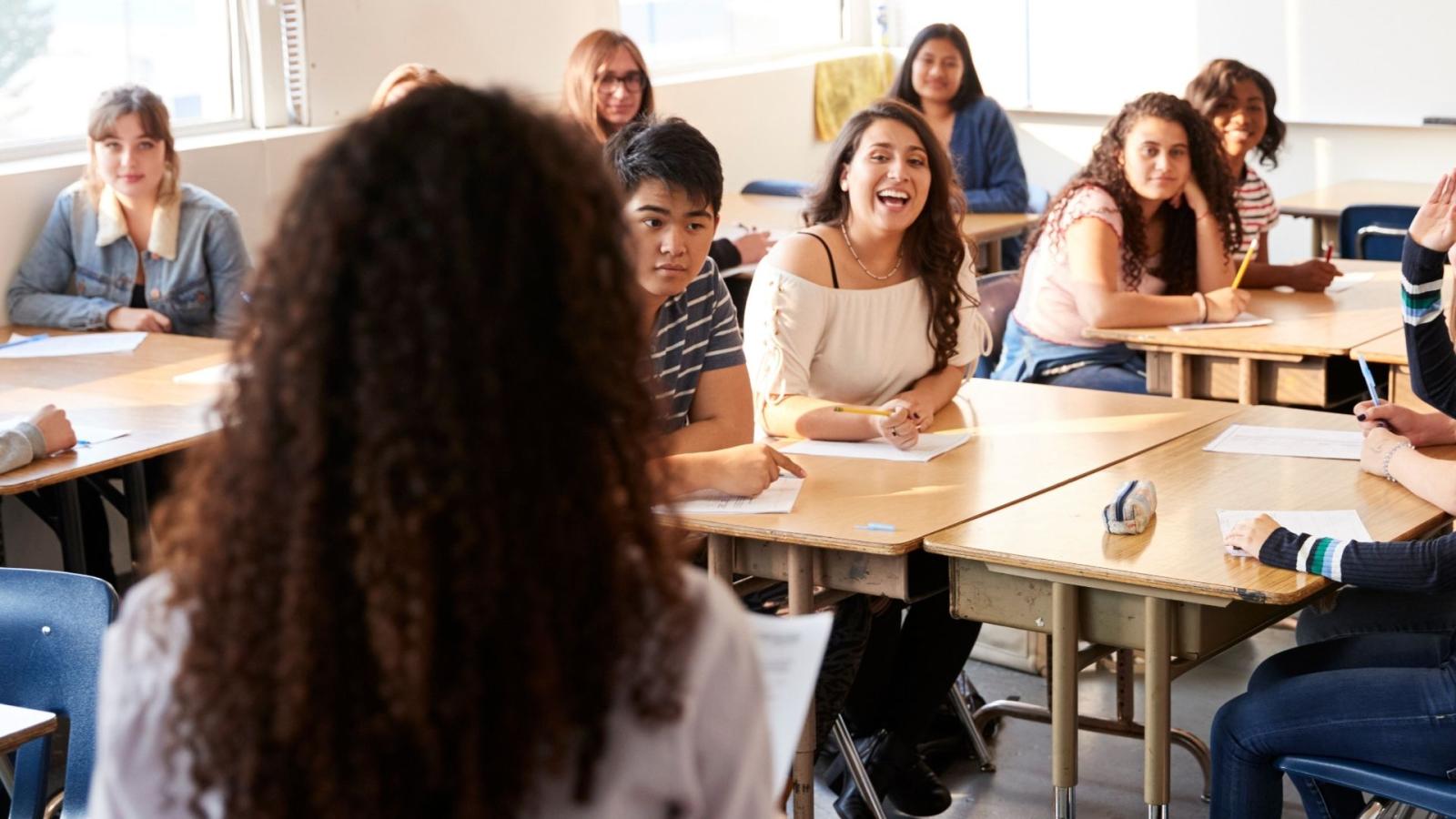 The back of a teacher's head as she faces out to a class of students all smiling