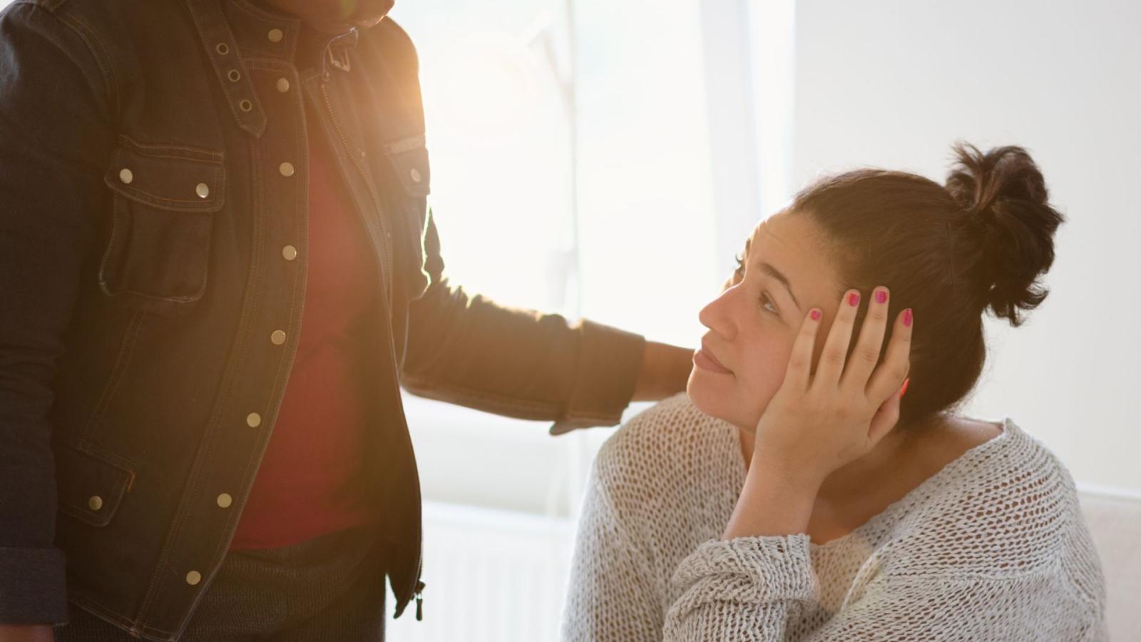 A young woman sitting down, being comforted by an older person