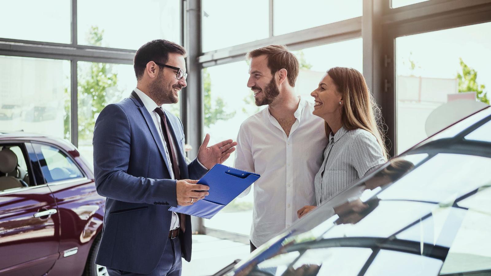 A man in a suit handing car keys to a couple in a car dealership