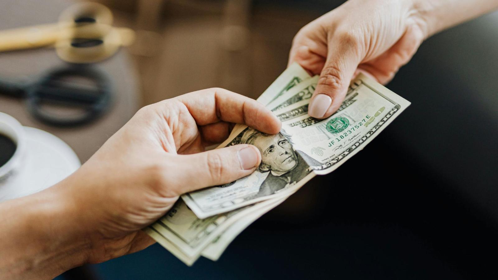 Close up of one hand passing another hand dollars