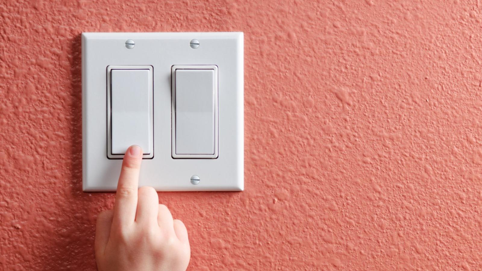 Close up of a small hand pressing a light switch with a pink painted wall