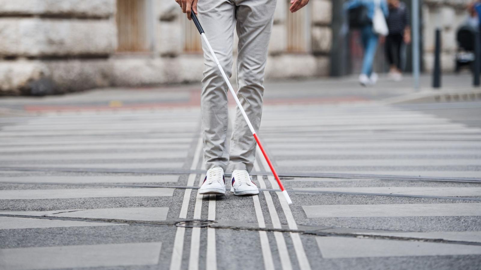 A visually impaired person uses a walking along a path with grooves, using their white cane to guide them