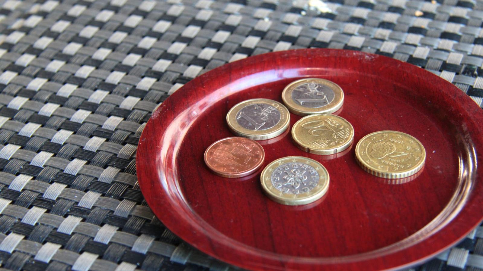 A couple of euro coins placed on a small red plate representing a tip in a restaurant